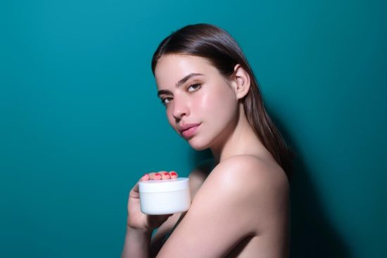 young-woman-applying-body-cream-against-studio-background-beauty-routine-studio-face-beautiful_265223-104263